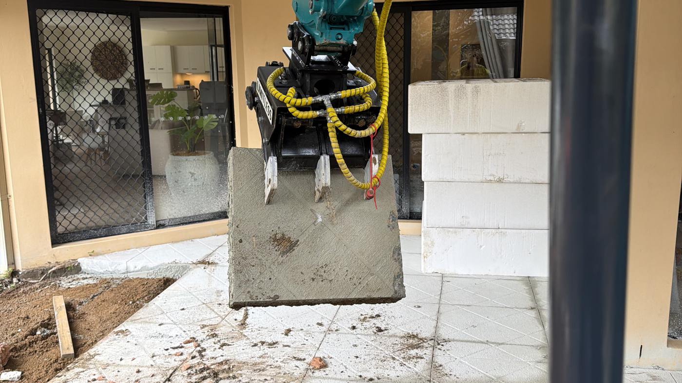A sawn slab section lifted clear of a house on the excavator