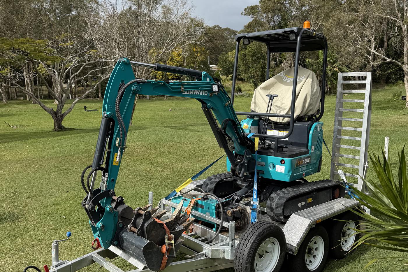 The 2026 Sunward 1.8-tonne mini excavator loaded on its trailer, buckets stacked on the drawbar