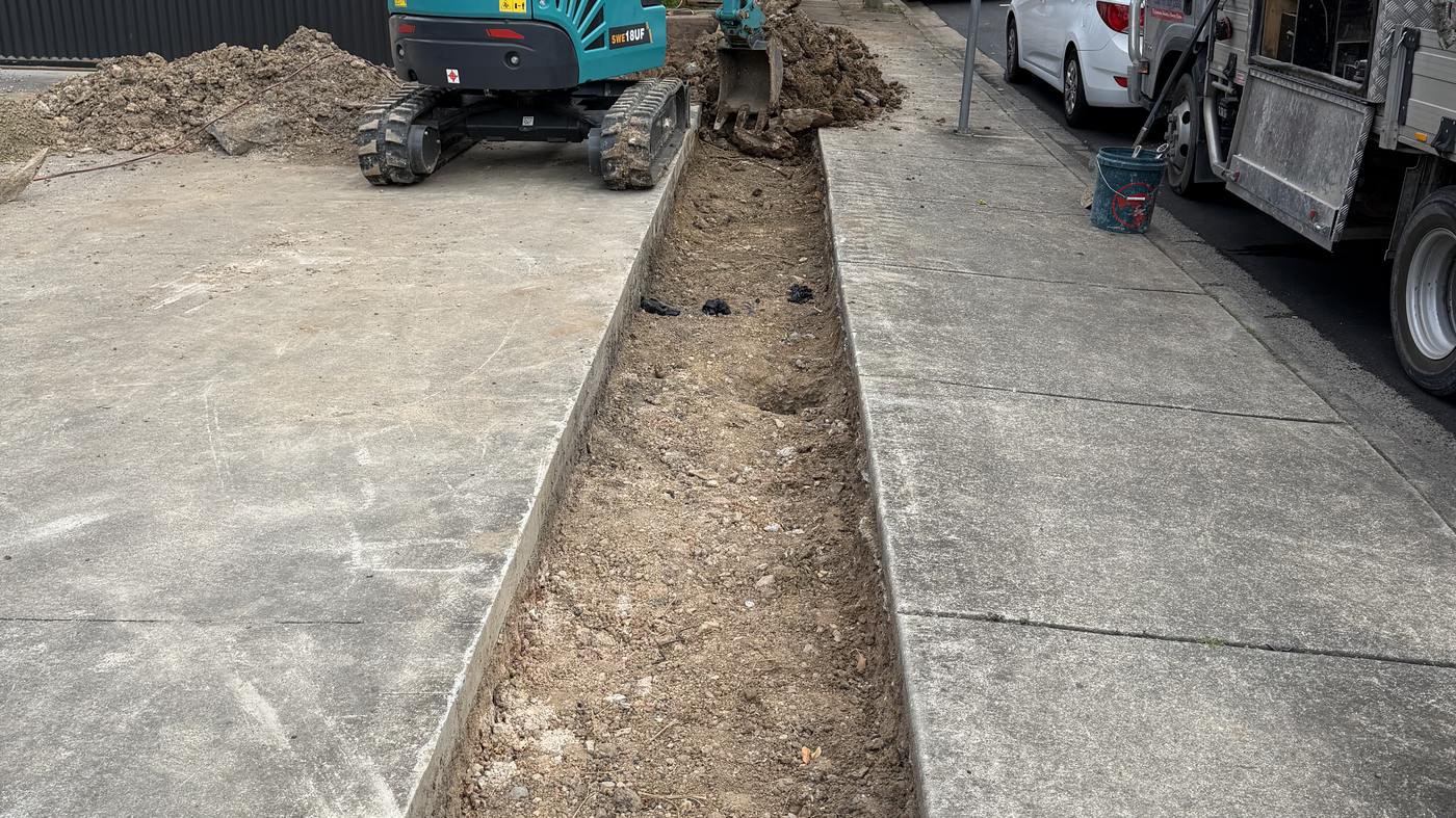 A trench cut out along the edge of a concrete driveway with the 1.8T at the far end and a tipper waiting